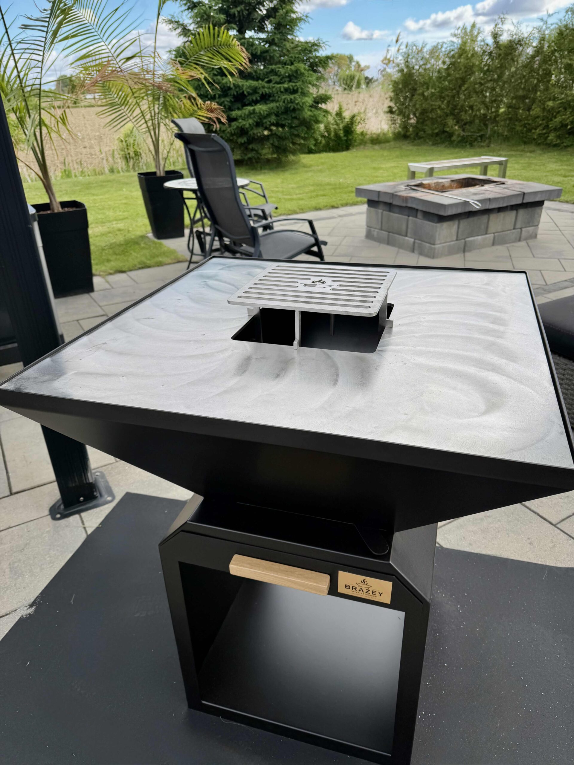 Outdoor stainless steel grilling station on a black pedestal with a metal vent cover, set on a patio.